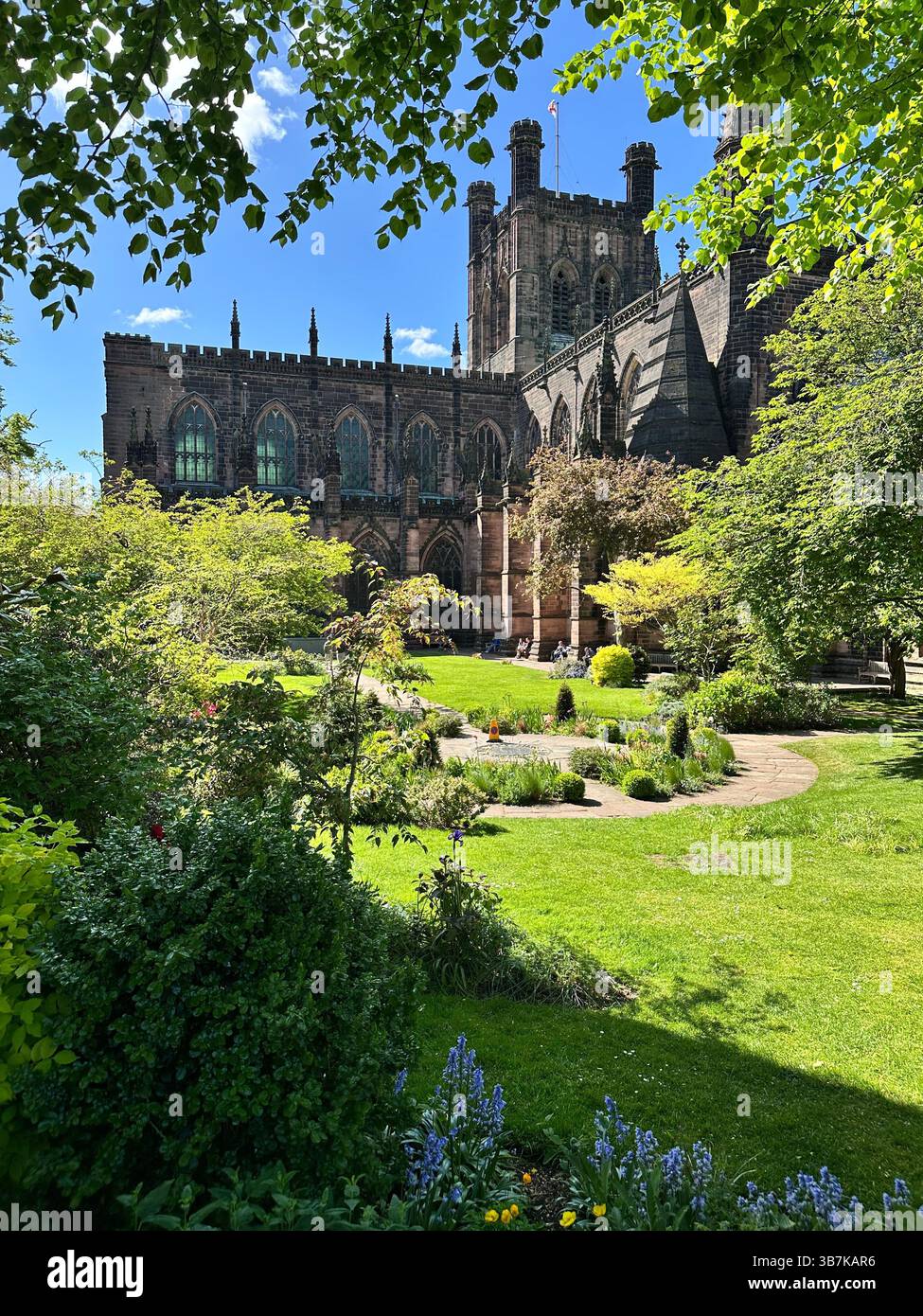 Low angle view of Chester Cathedral and its gardens on a sunny day, with bright blue skies and historic architecture. - Smartphone Captured Stock Image