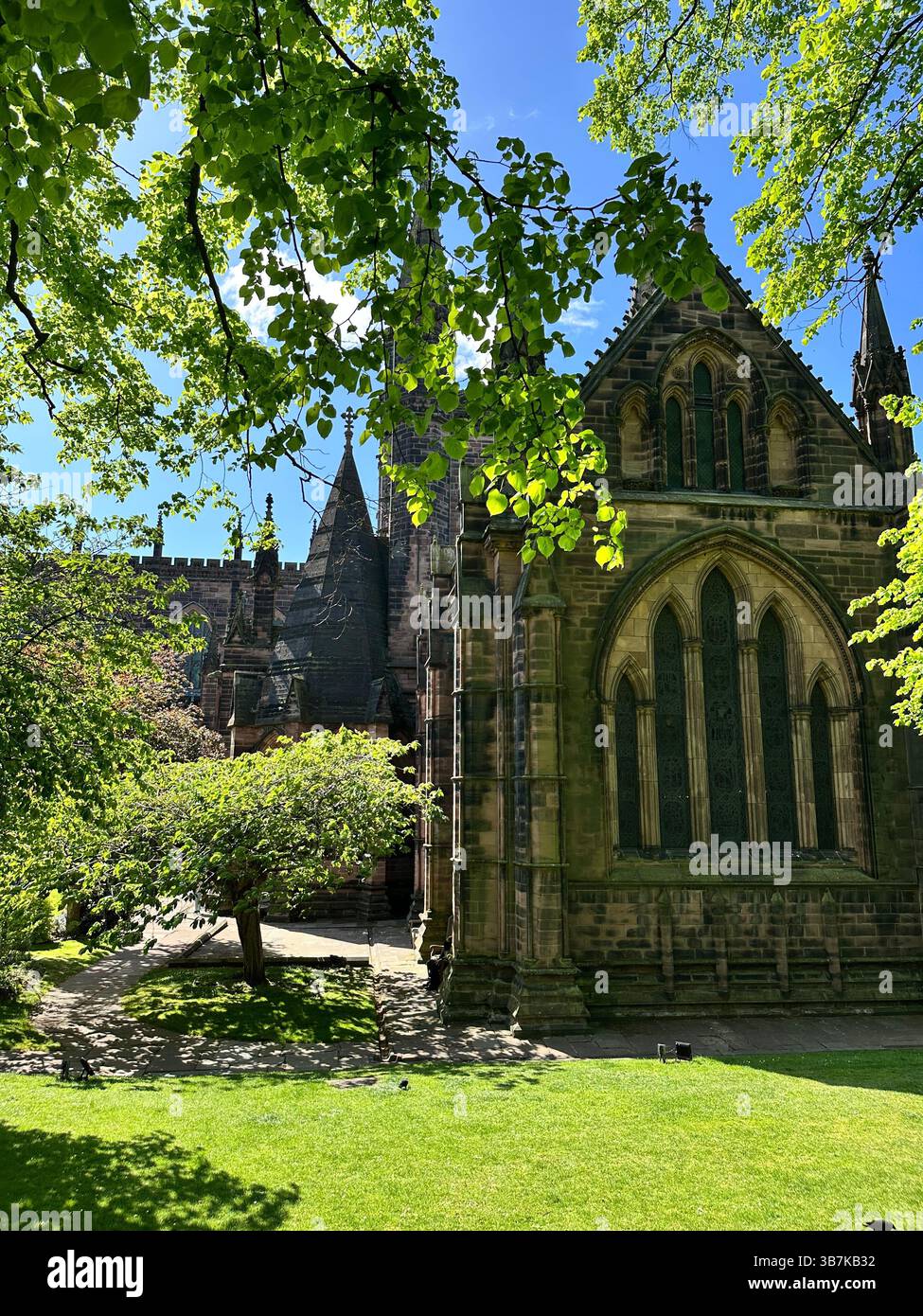 Low angle view of Chester Cathedral and its gardens on a sunny day, with bright blue skies and historic architecture. - Smartphone Captured Stock Image