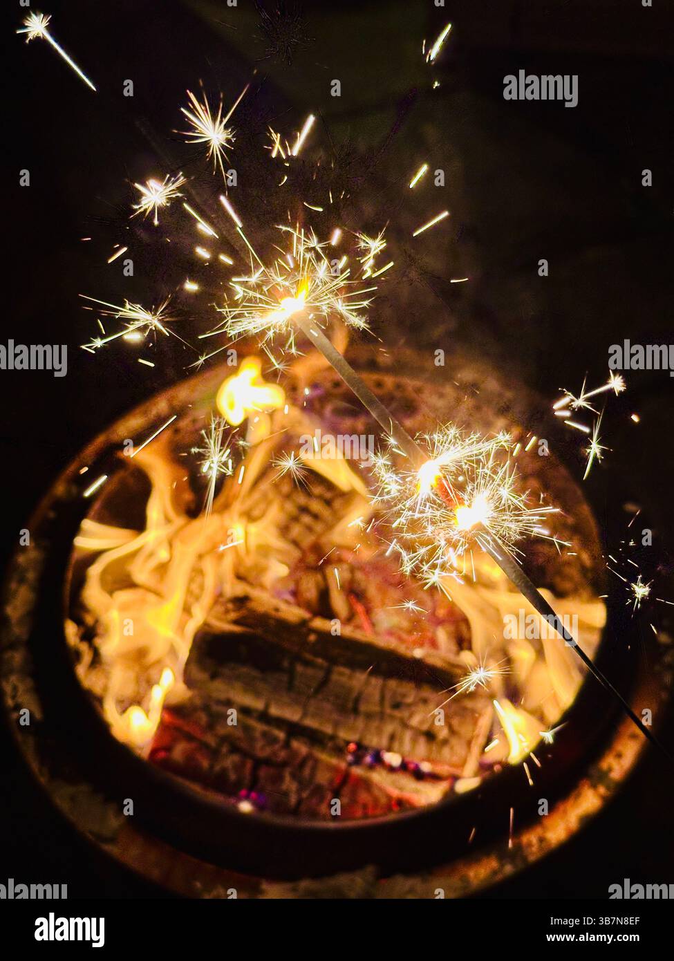Lit sparklers over an outdoor burning fire pit at nightime - Smartphone Captured Stock Image
