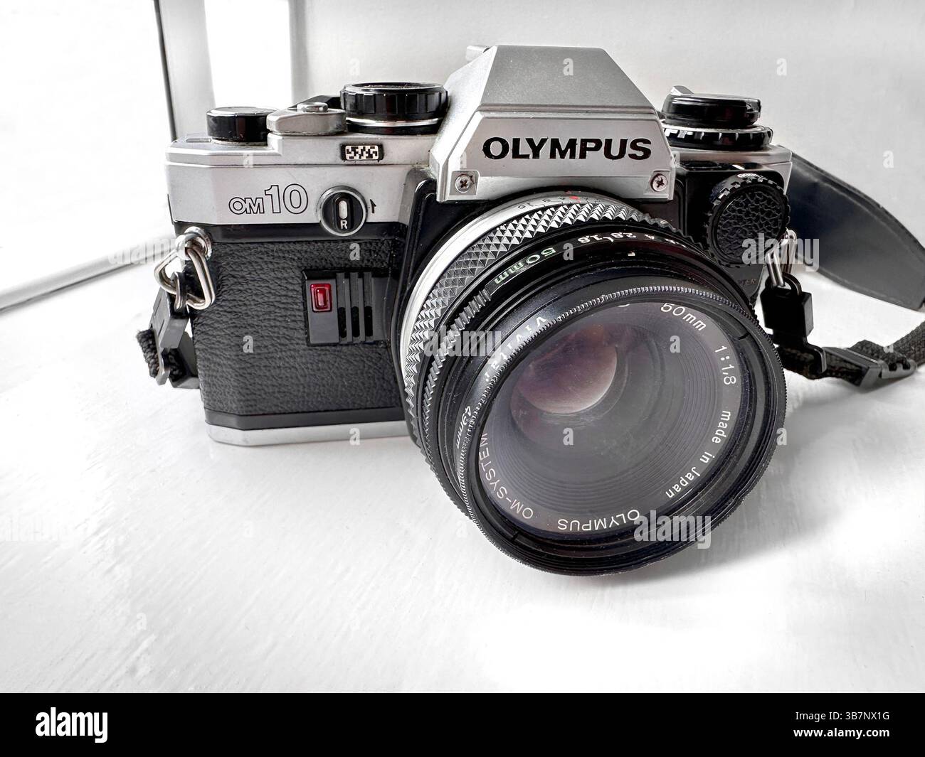 Close-up of a vintage Olympus OM10 film camera with a Zuiko lens set on a white surface near a window - Smartphone Captured Stock Image