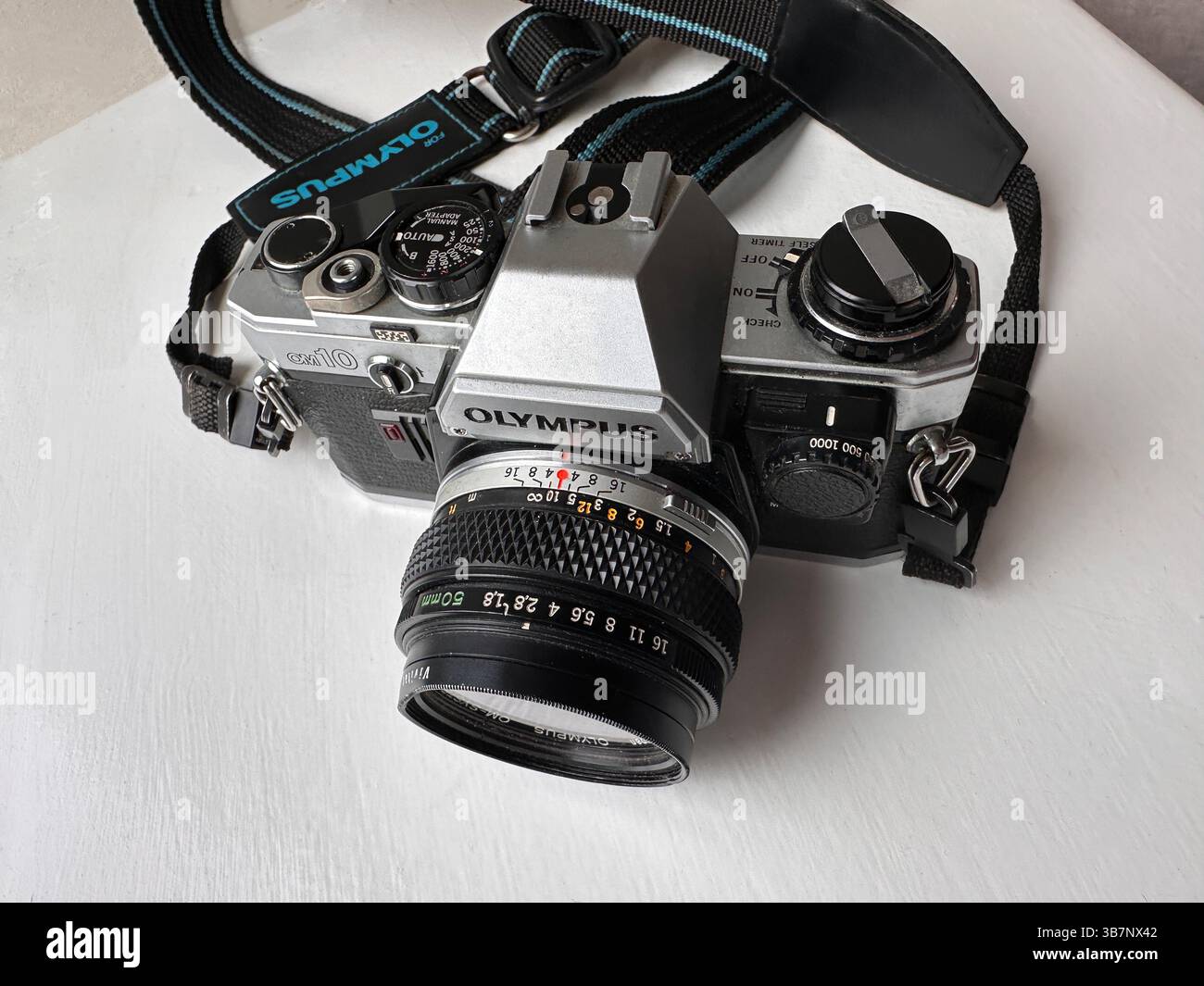 Close-up of a vintage Olympus OM10 film camera with a Zuiko lens set on a white surface near a window - Smartphone Captured Stock Image