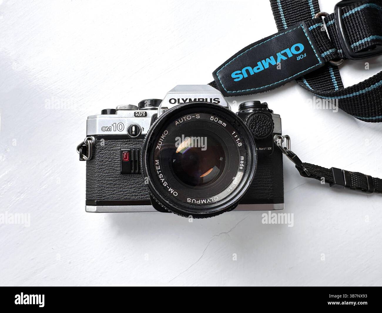 Close-up of a vintage Olympus OM10 film camera with a Zuiko lens set on a white surface near a window - Smartphone Captured Stock Image