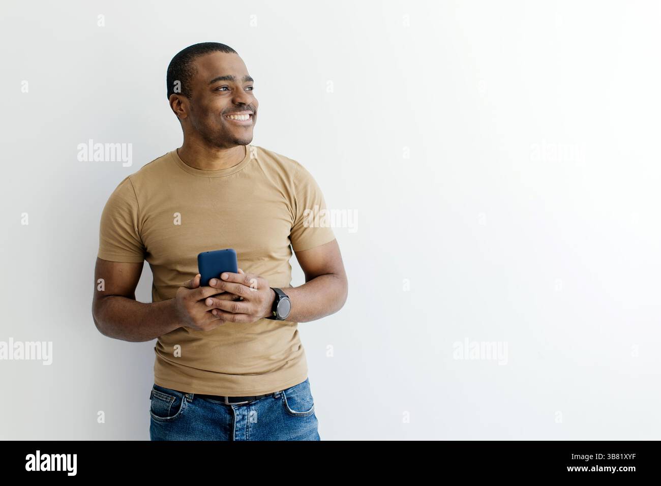 Smiling African American man holding smartphone while looking aside at copy space Stock Photo