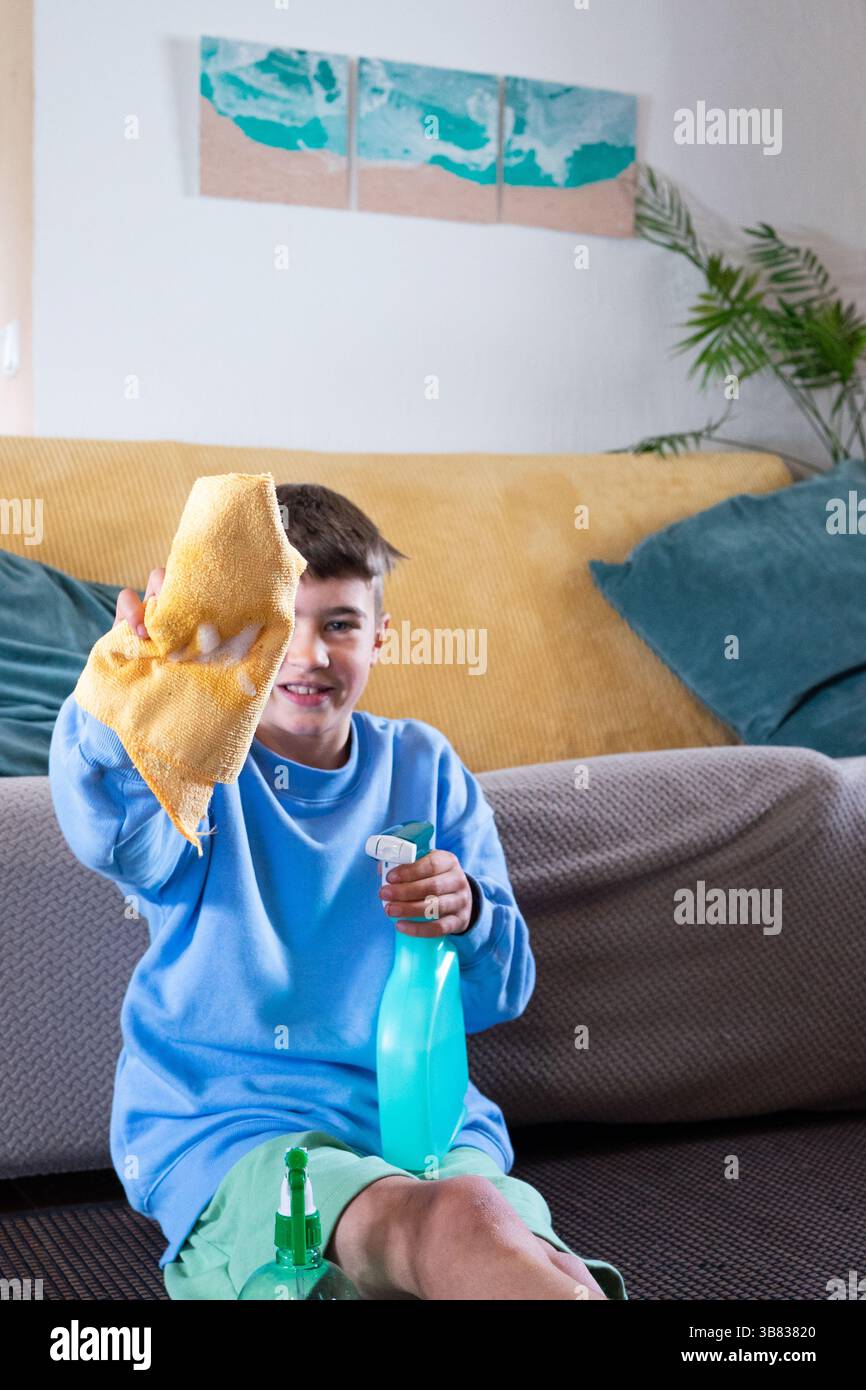 Young boy holding cleaning supplies and cleaning cloth, ready to clean house Stock Photo