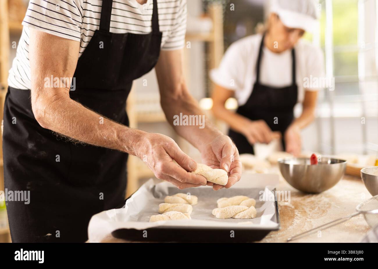 Baker's hands fold pieces of dough on baking sheet Stock Photo