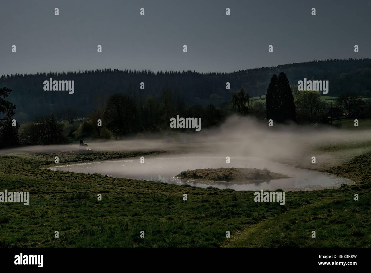 Mist hangs in the air above a pond on a clear cold moonlit night, photographed by the light of the full moon (Presteigne, Powys, UK) Stock Photo