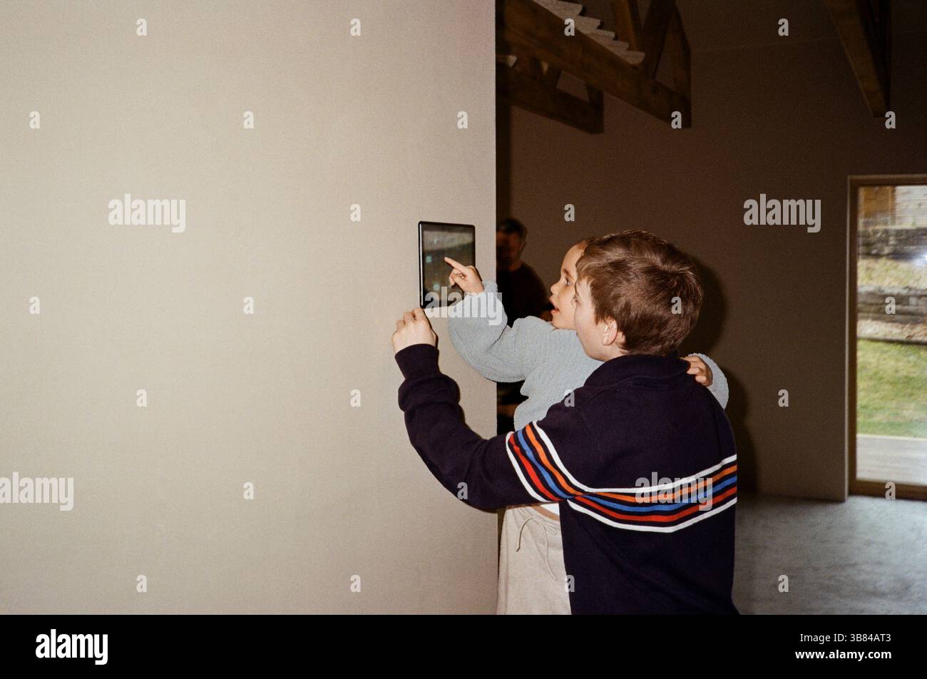 Siblings operating tablet PC mounted on wall at home Stock Photo