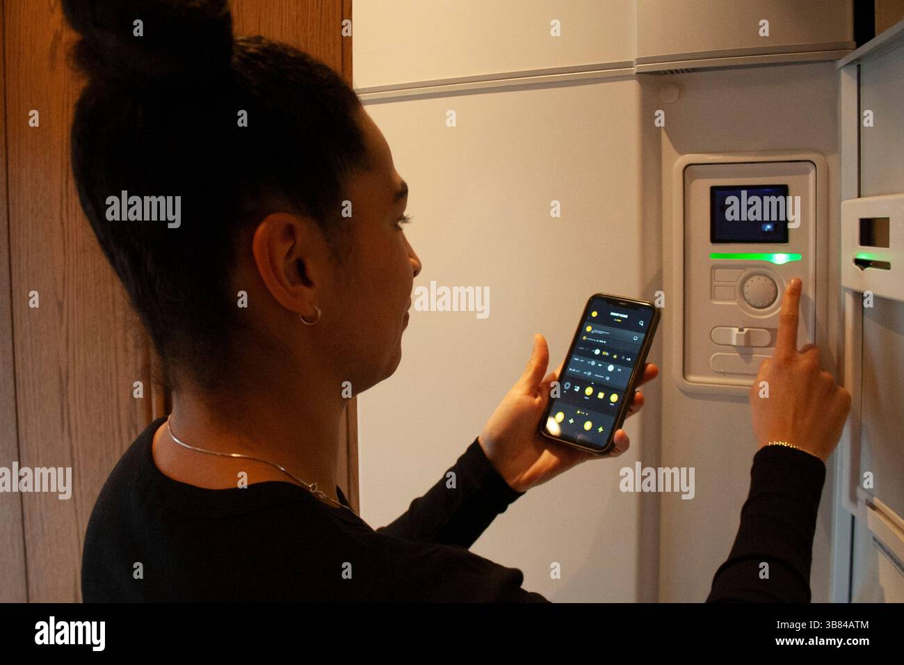 Woman connecting smart phone app with thermostat at home Stock Photo