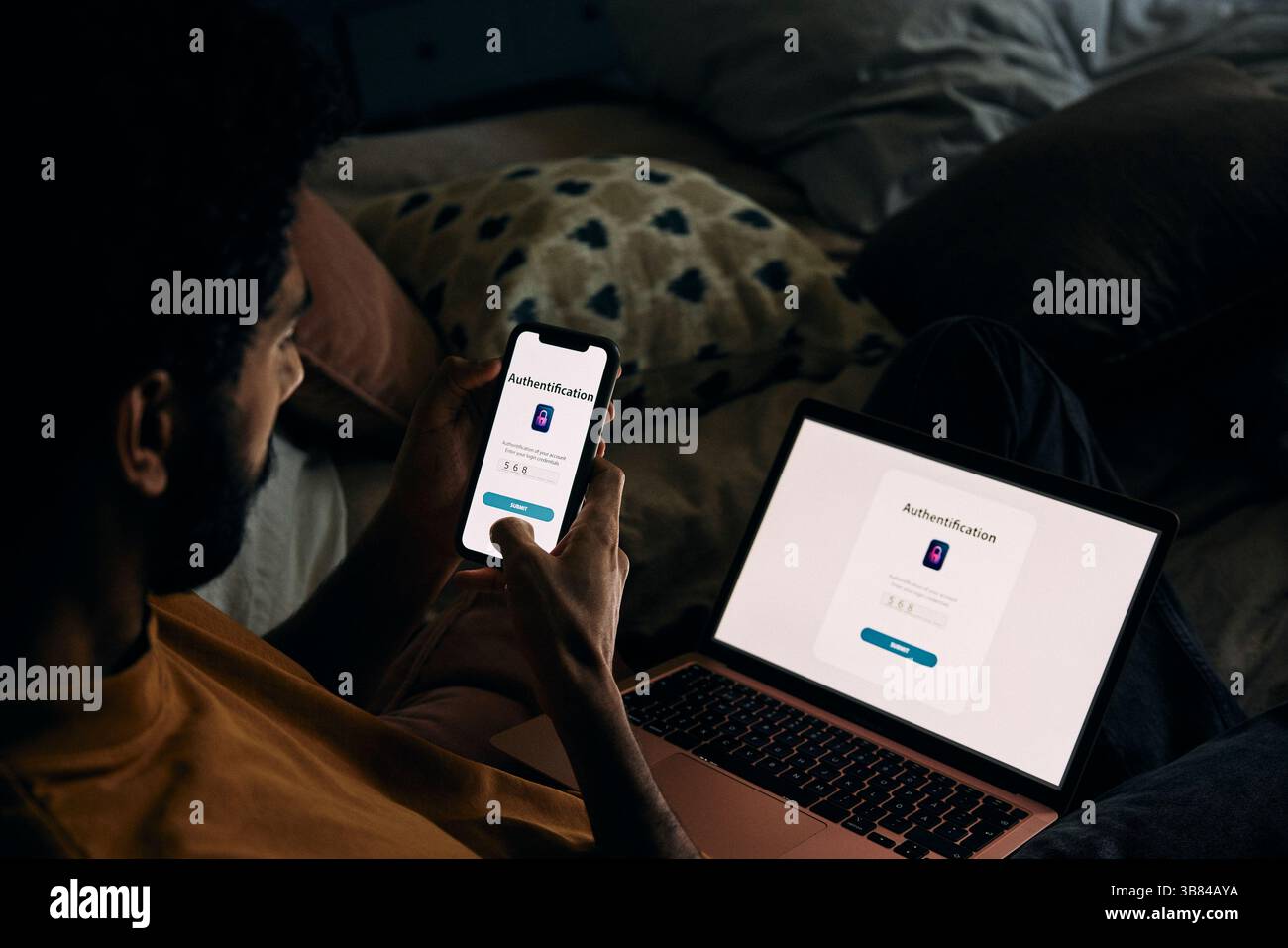 Man accessing laptop through smart phone with authentication password while sitting in bedroom at home Stock Photo