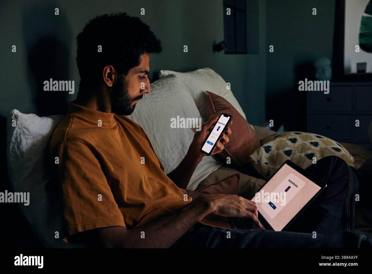 Man typing authentication password on laptop from smart phone while sitting in bedroom at home Stock Photo