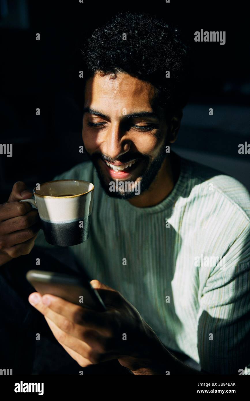 Happy man drinking coffee while using smart phone Stock Photo