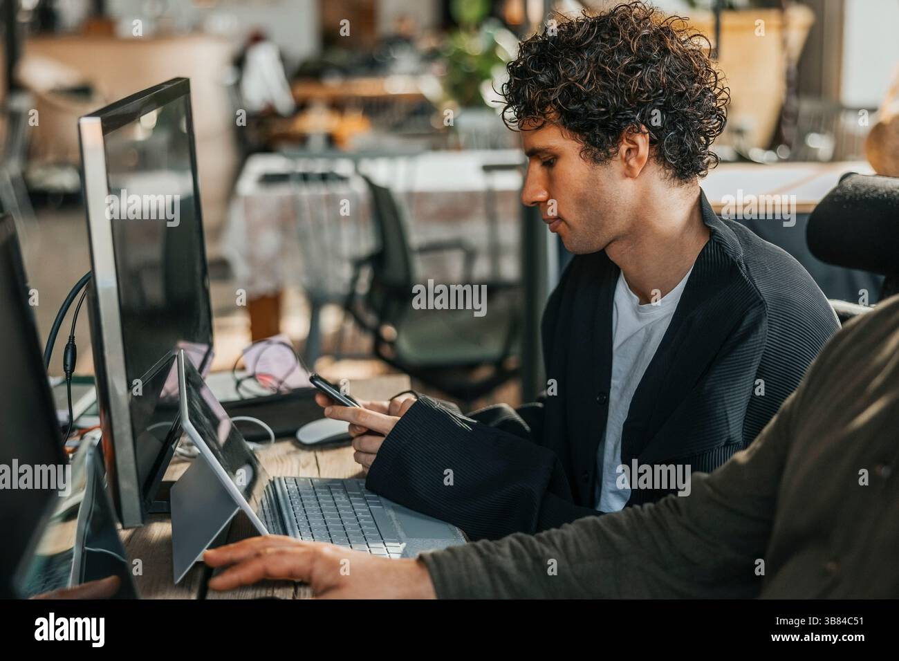 Male computer programmer using smart phone while sitting with wireless technologies in office Stock Photo