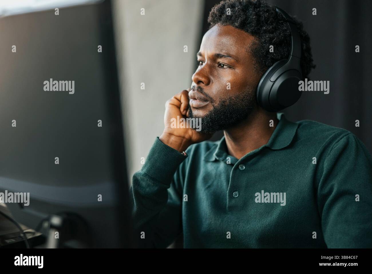 Male computer programmer wearing wireless headphones leaning on elbow ...