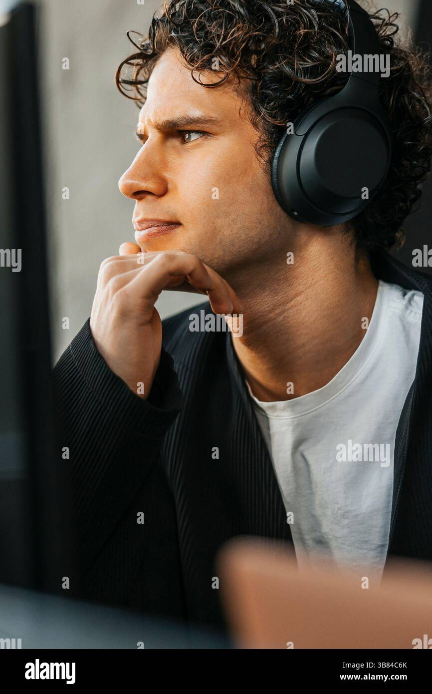 Tilted image of focused young computer programmer wearing wireless headphones looking at computer while working in offic Stock Photo