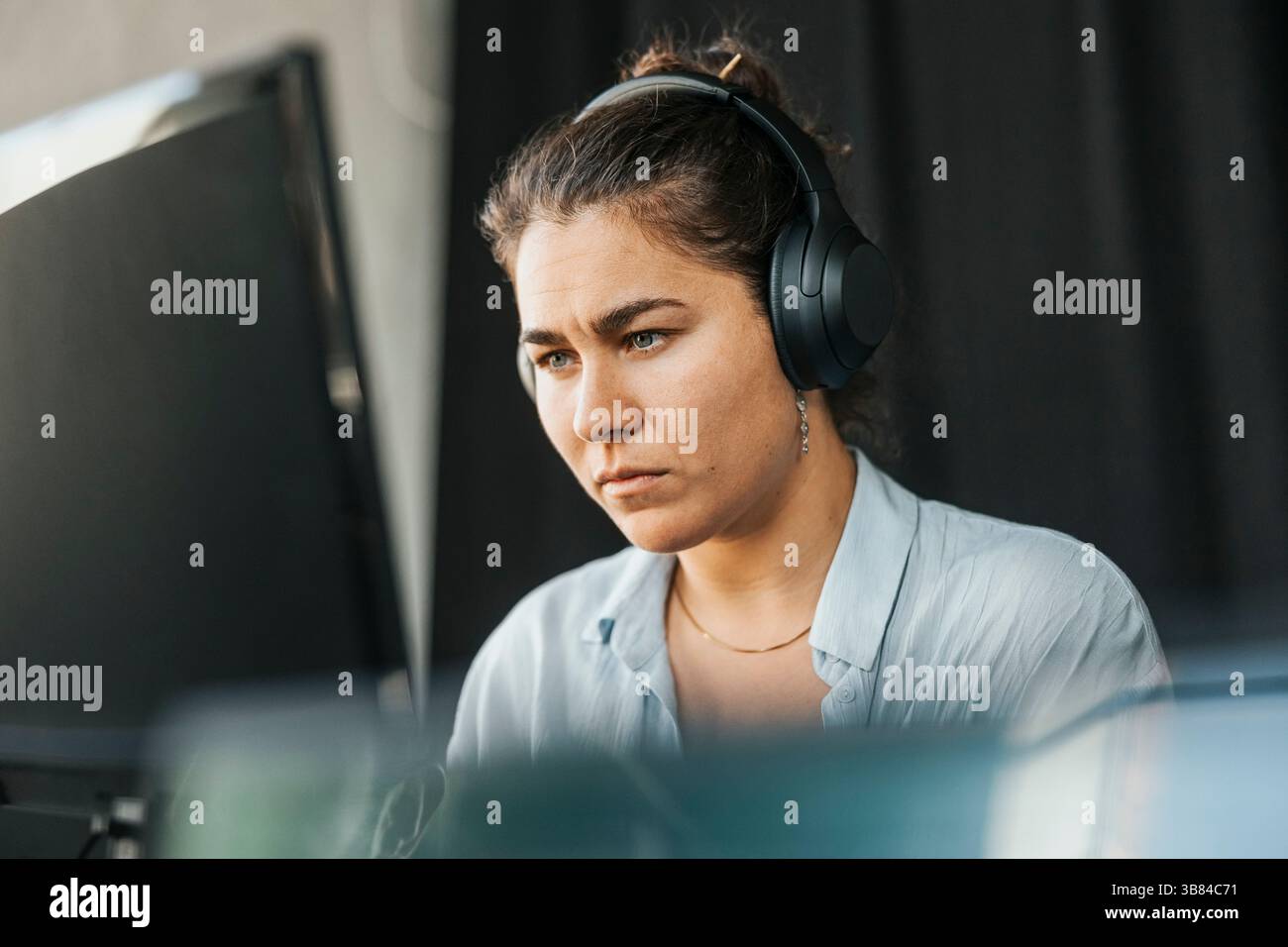 Focused young female programmer wearing wireless headphones using computer in office Stock Photo