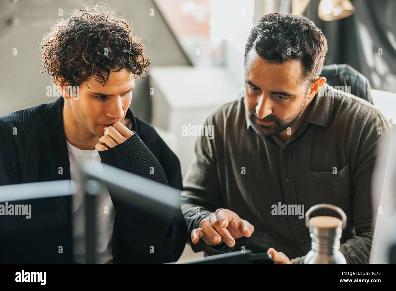 Male computer programmers discussing ideas on smart phone while sitting in office Stock Photo
