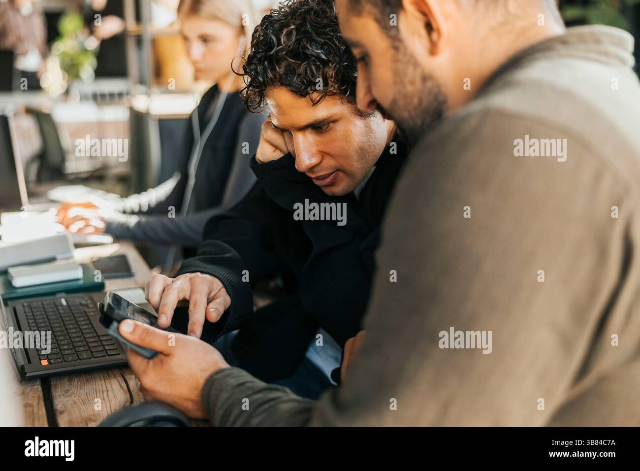 Male software engineers using smart phone while discussing strategies in tech office Stock Photo