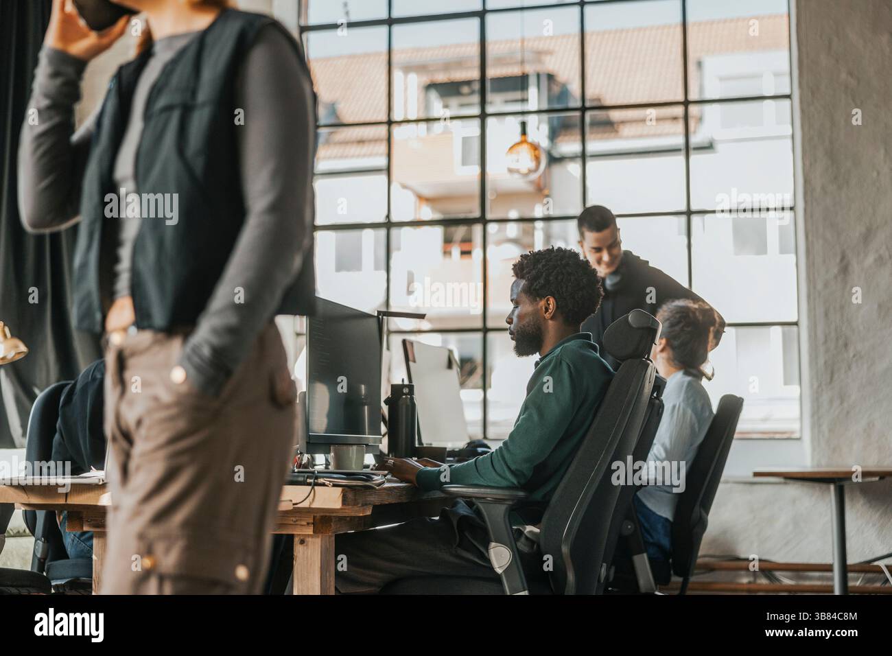 Focused male computer programmer coding on desktop PC while sitting at desk in tech hub Stock Photo