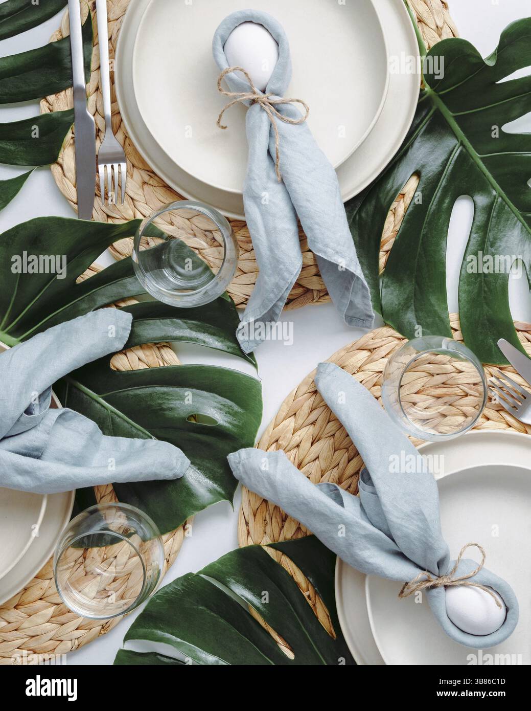 Tropical Easter Tablesetting. Top view of table setting for Christian Easter with bunny eggs decorated monstera leaves. Aesthetic Easter tablescapes. Stock Photo