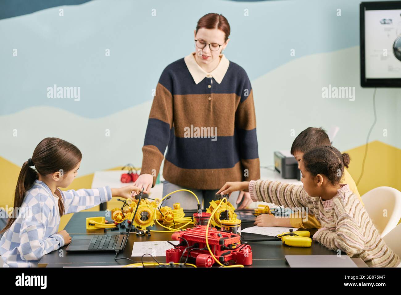 Teacher guiding students in robotic programming class using various educational kits. Children engaged in interactive learning with robotic devices on Stock Photo
