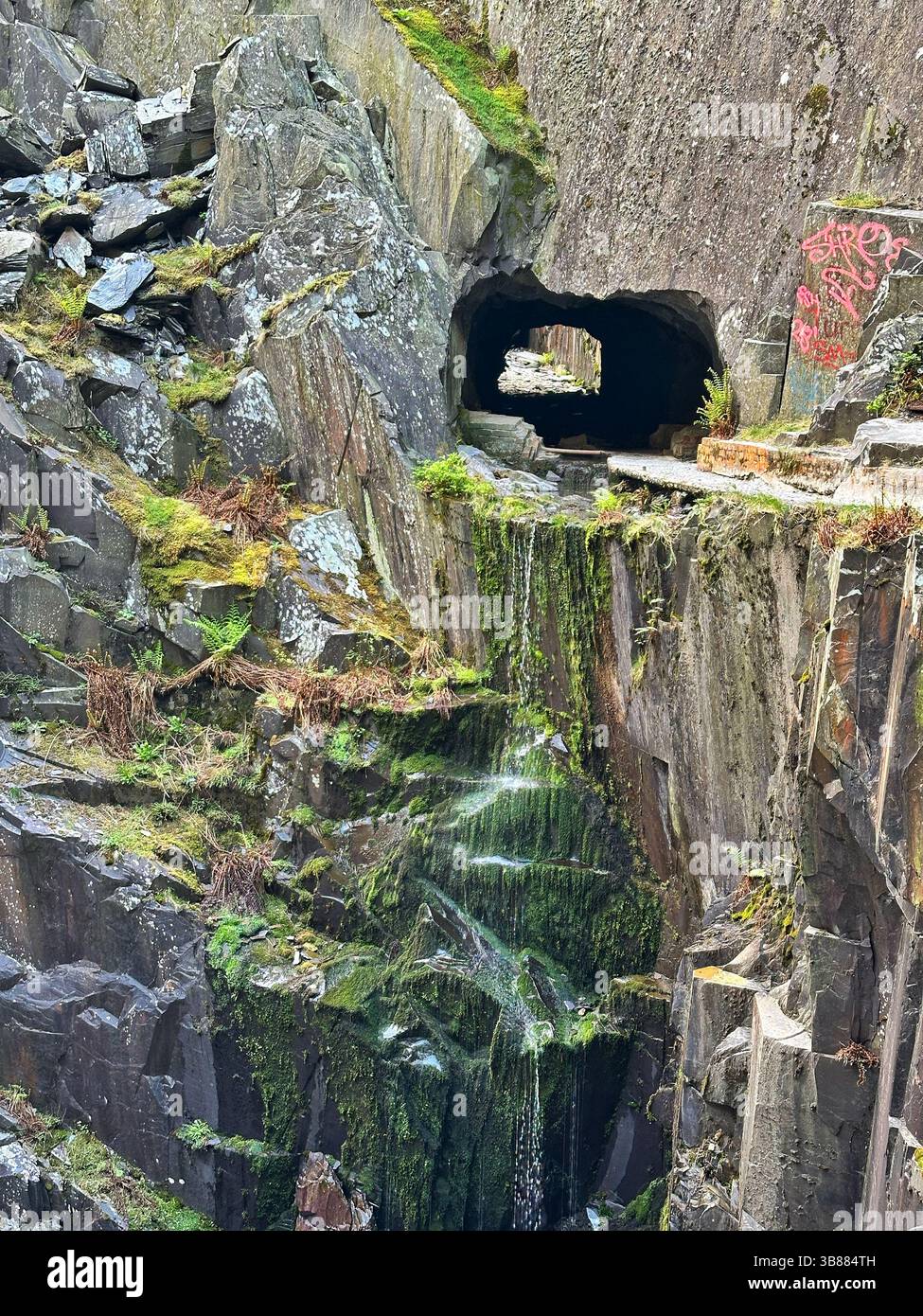 Moss covered rocks and trickling water in the centre of Dinorwic Quarry with the rock tunnel in view, near Llanberis, Snowdonia, Wales, UK. - Smartphone Captured Stock Image
