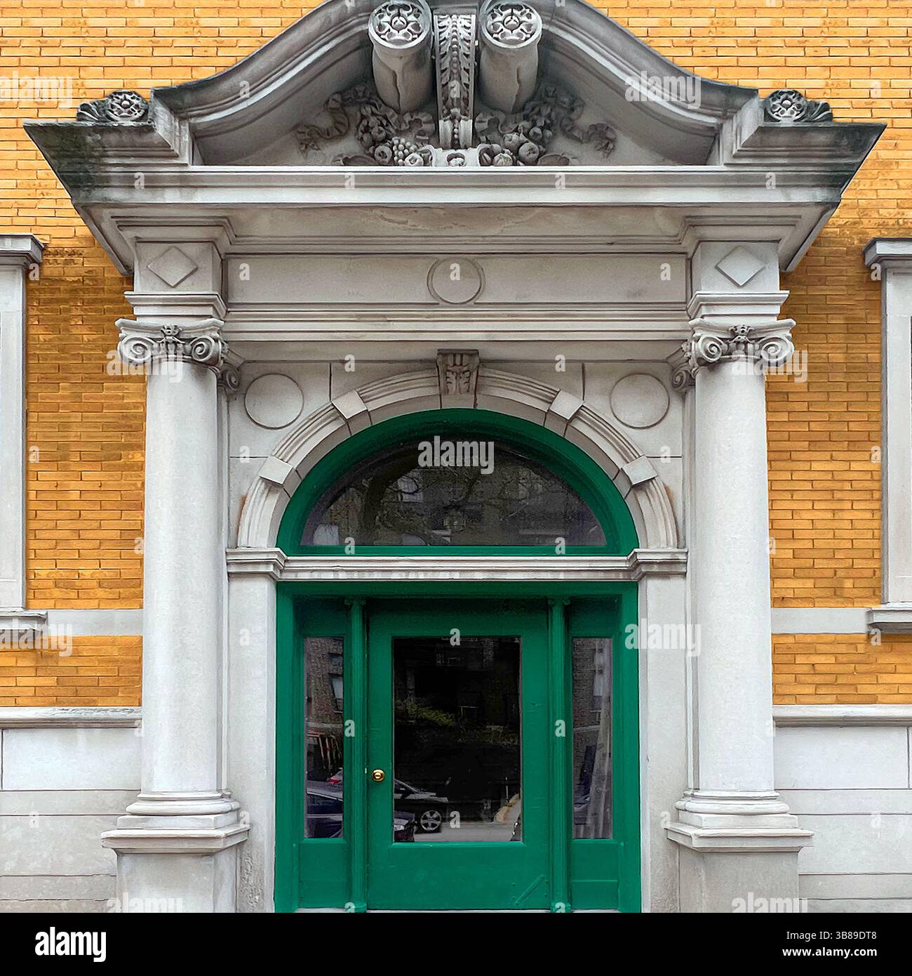 Grand neoclassical entrance with ornate pediment, Corinthian columns, and a green arched door set into a yellow brick facade in Chicago - Smartphone Captured Stock Image