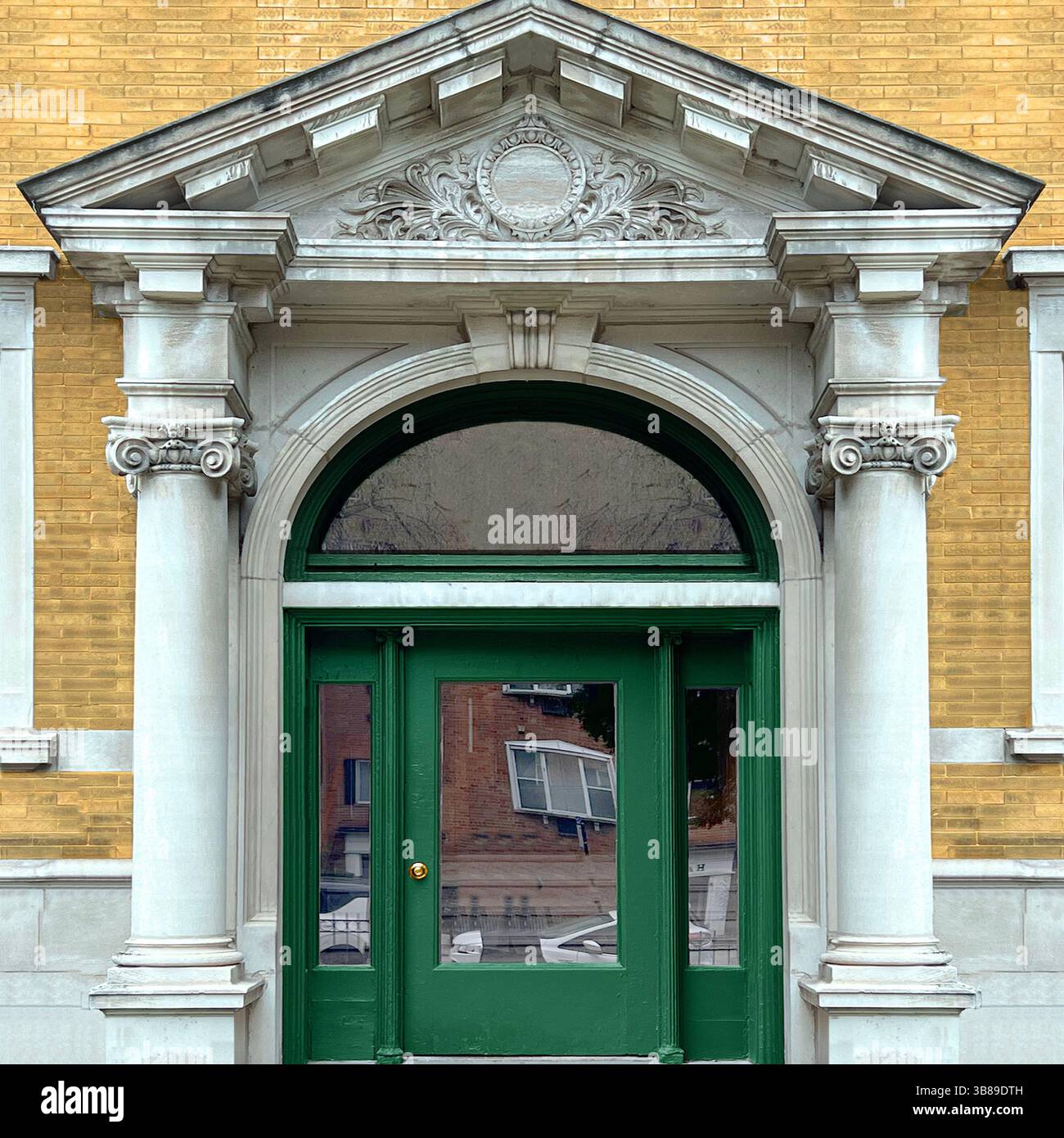 Classical architectural entrance with Corinthian columns, a green arched door, and a detailed triangular pediment on a yellow brick Chicago building - Smartphone Captured Stock Image
