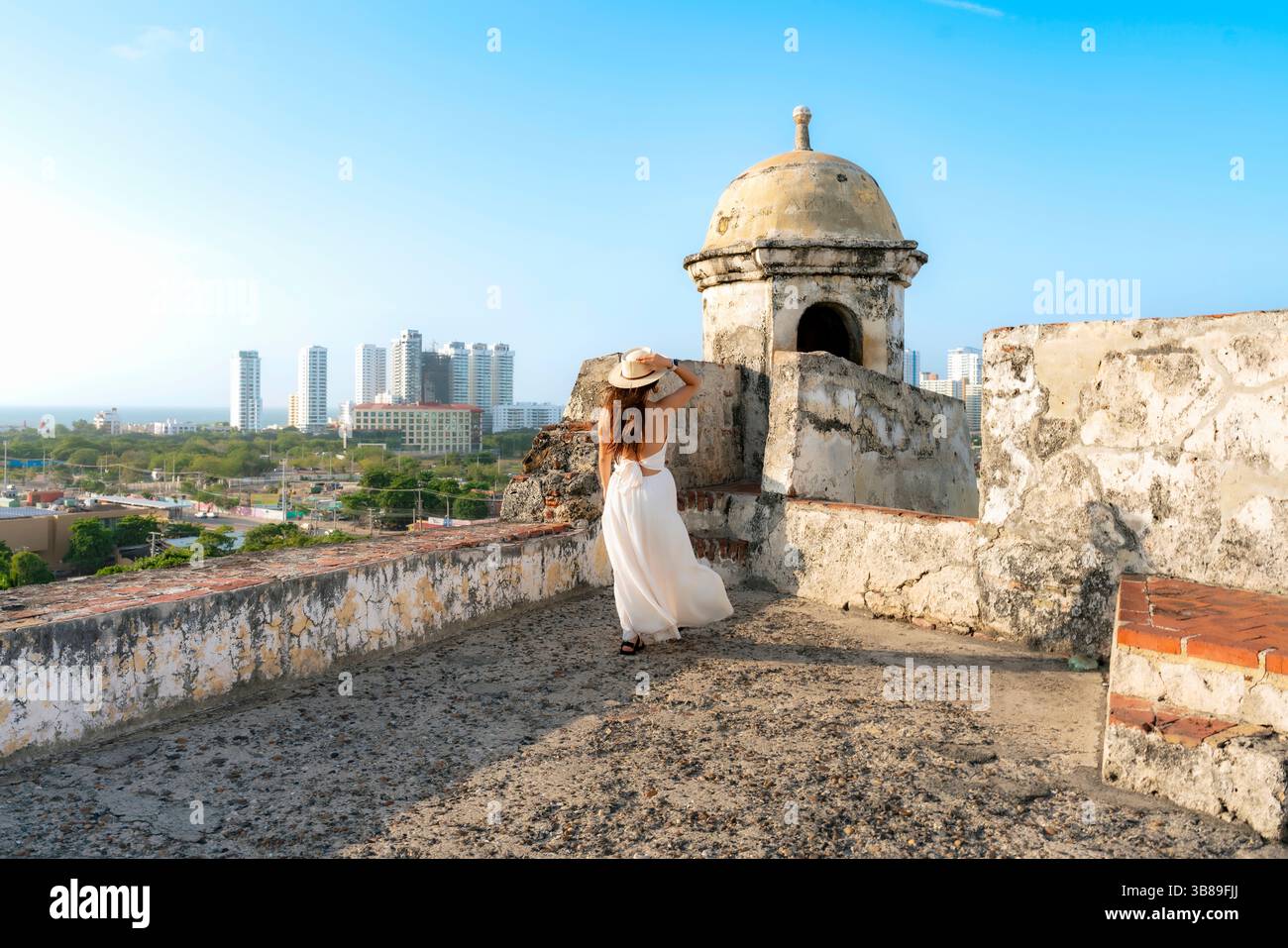 Taken at sunset in Cartagena, Colombia, a Unrecognized young Latina woman in a white dress and hat walks through San Felipe Castle, enjoying the breez Stock Photo