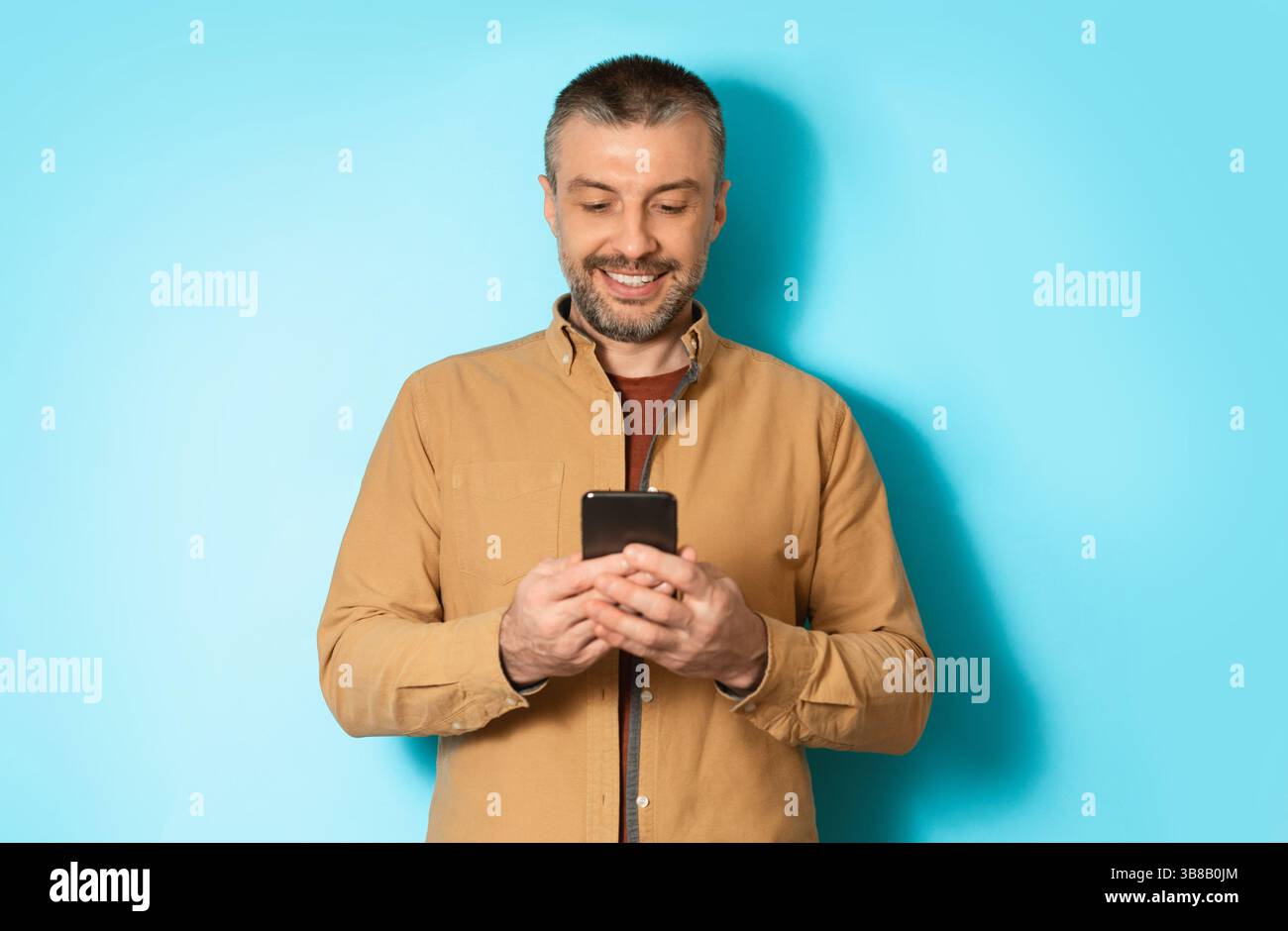 Cheerful Man Using Mobile Application On Cellphone Over Blue Background Stock Photo
