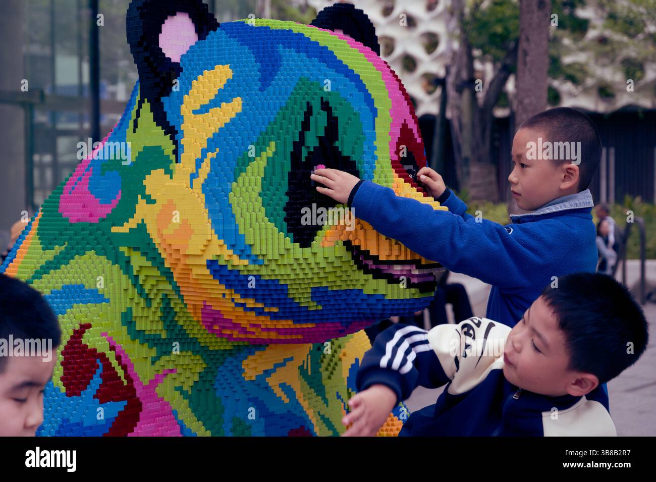 Children curiously touching a colorful, pixelated panda sculpture made from LEGO bricks Stock Photo
