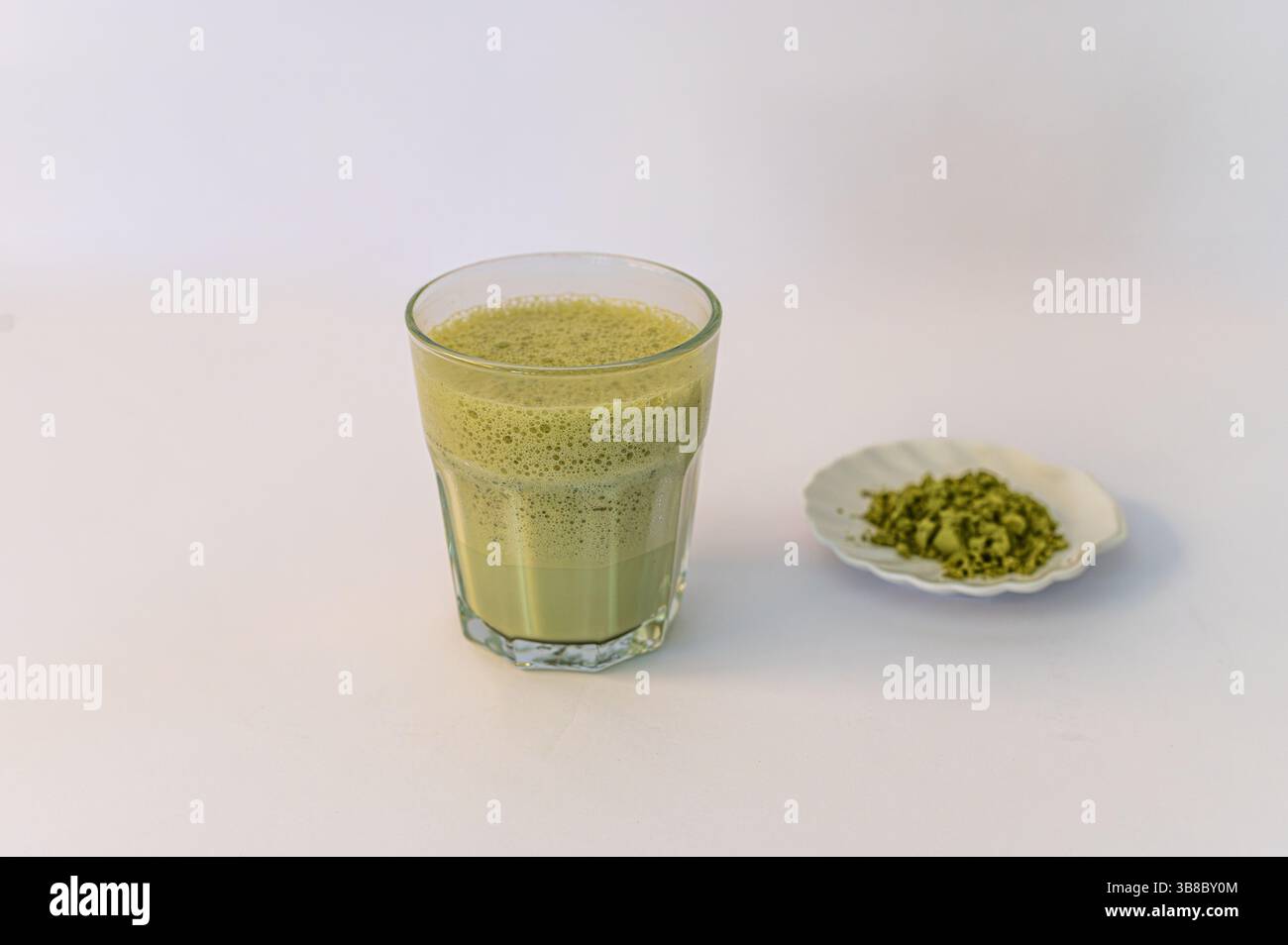 A vibrant green matcha drink alongside a bowl of fine matcha powder, presented on a clean white background for a fresh and minimalistic look. Stock Photo