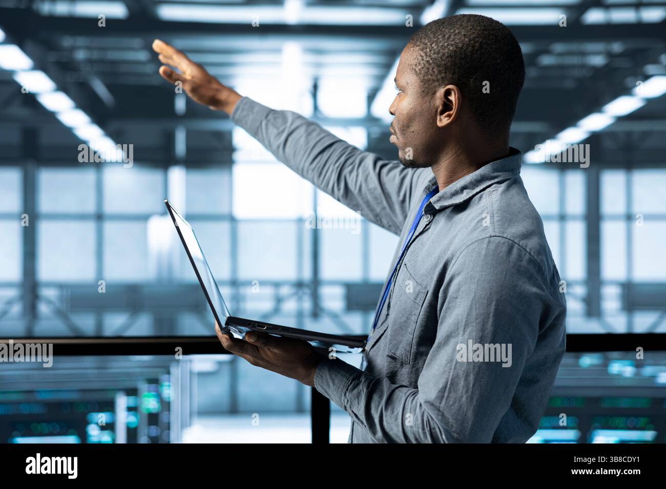 Technician holding laptop, looking around data center, managing server virtualization, finetuning network protocols, verifying high availability configurations, enforcing advanced security measures Stock Photo