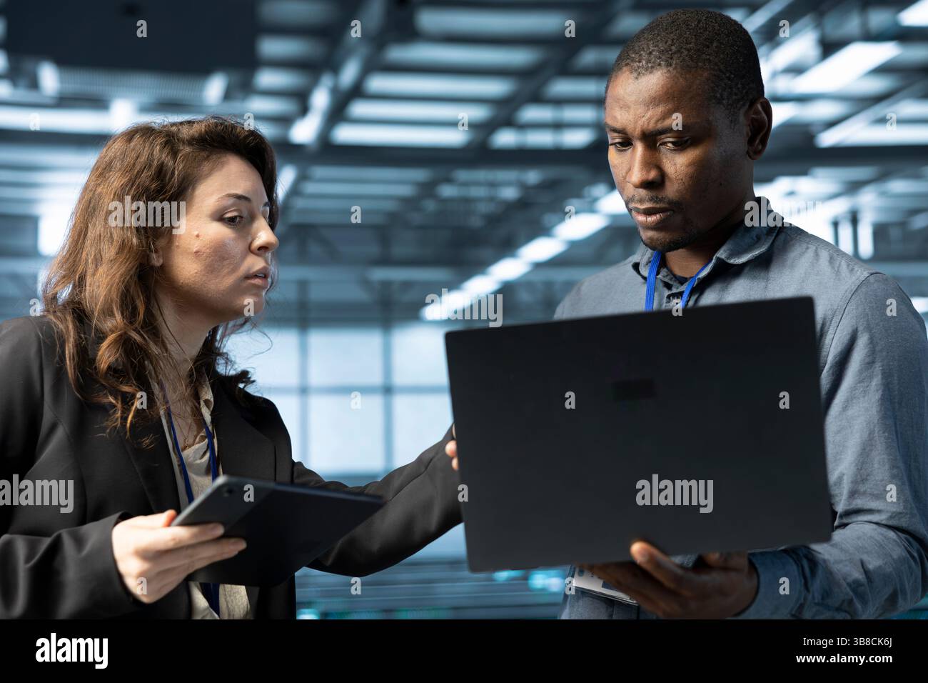 System administrators using laptop in data center, managing server virtualization. IT specialists using notebook in server room, sustaining long term infrastructure reliability Stock Photo