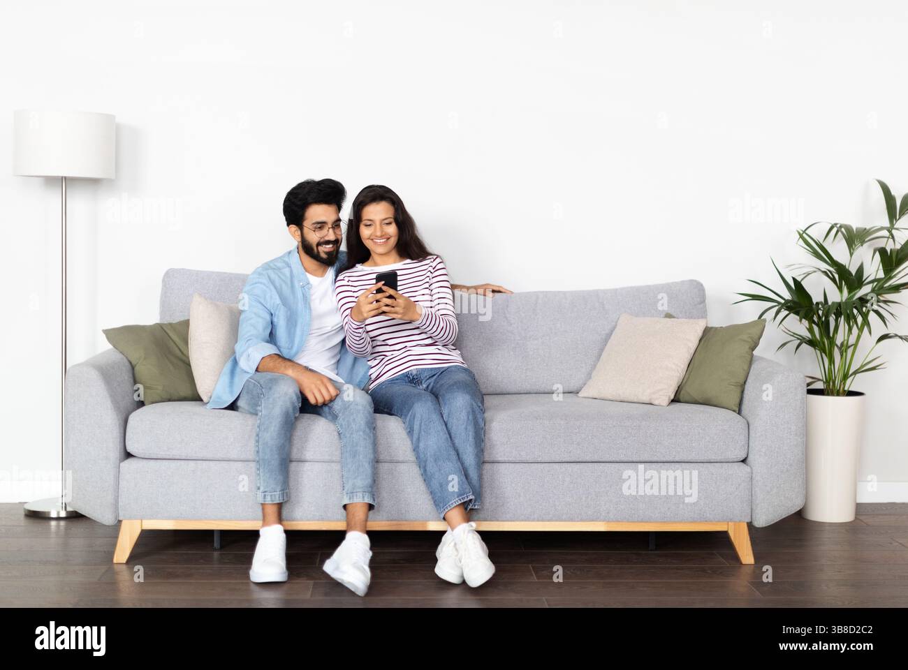 Relaxed multicultural couple sitting on sofa, using smartphone Stock Photo