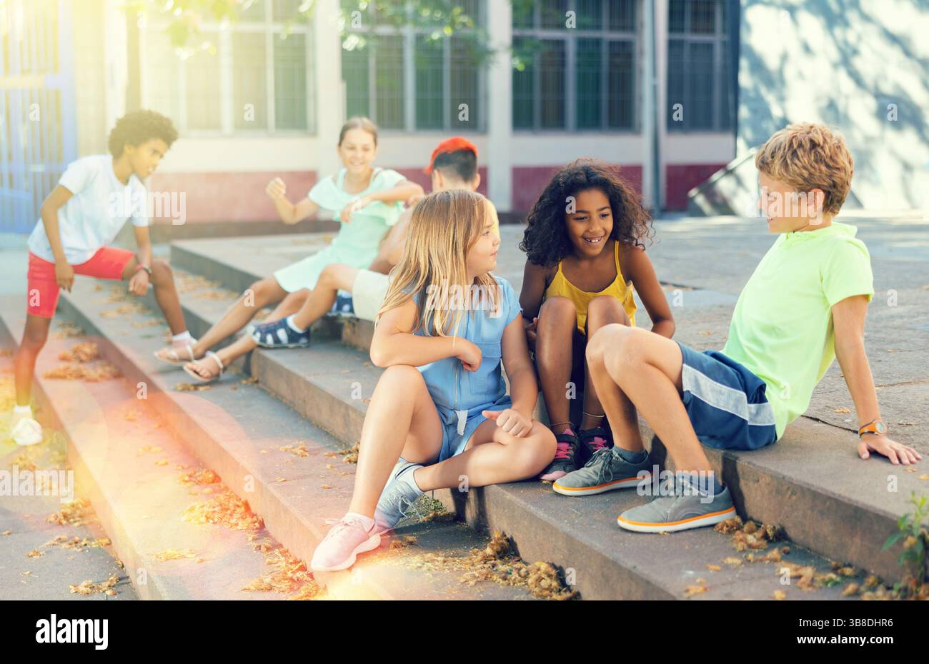Positive tweenagers friendly blabbing while sitting on steps outdoors Stock Photo