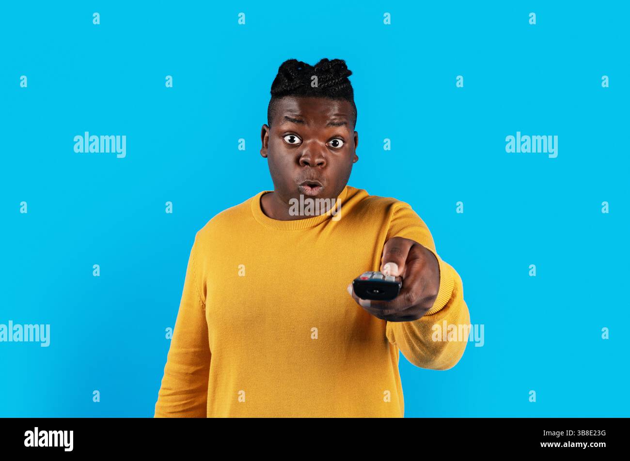 Shocked Black Man Watching Television, Pointing Remote Controller At Camera Stock Photo