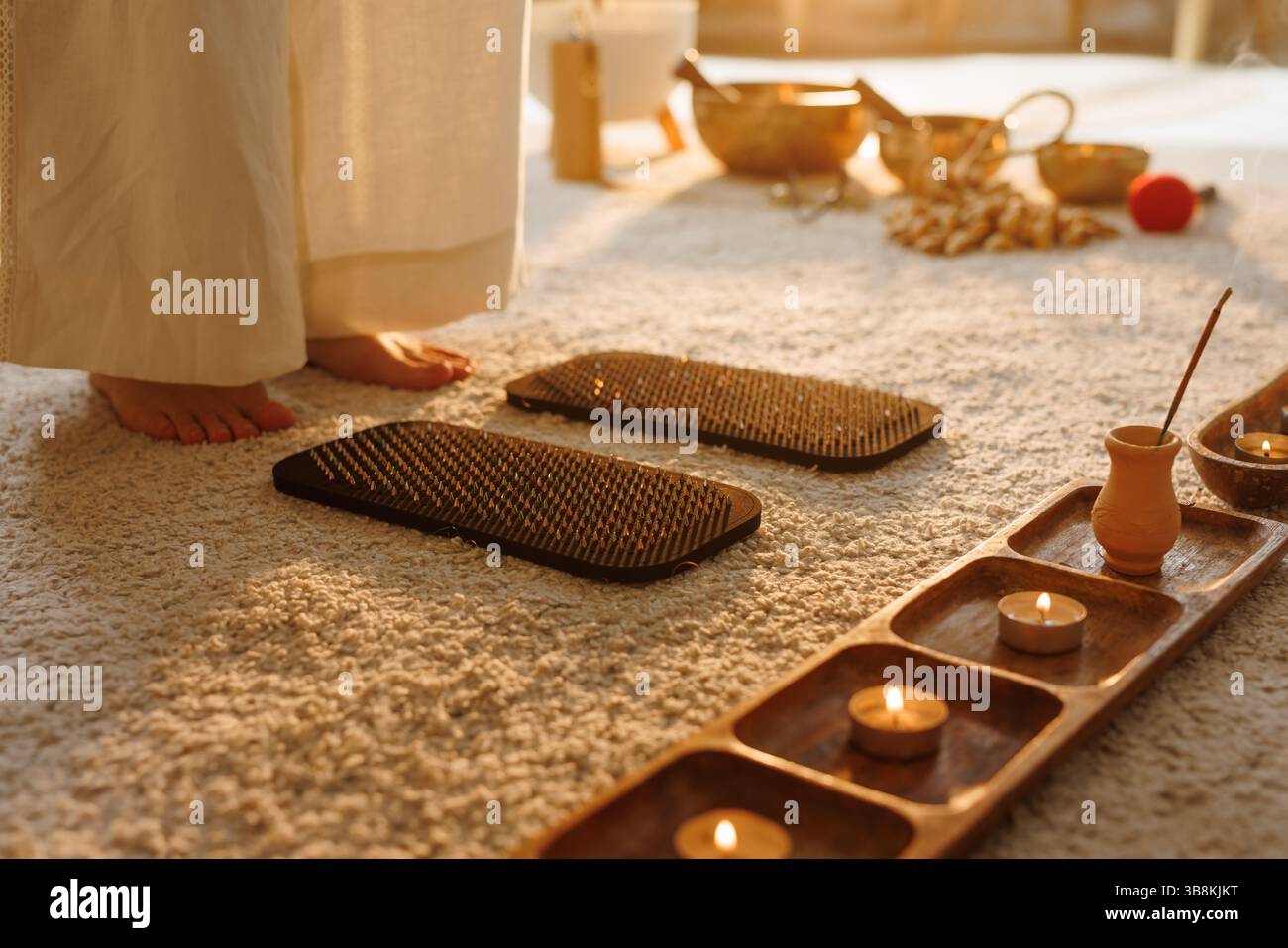 Barefoot woman preparing for nail board Sadhu meditation practice surrounded by incense, candles, and healing tools. Stock Photo