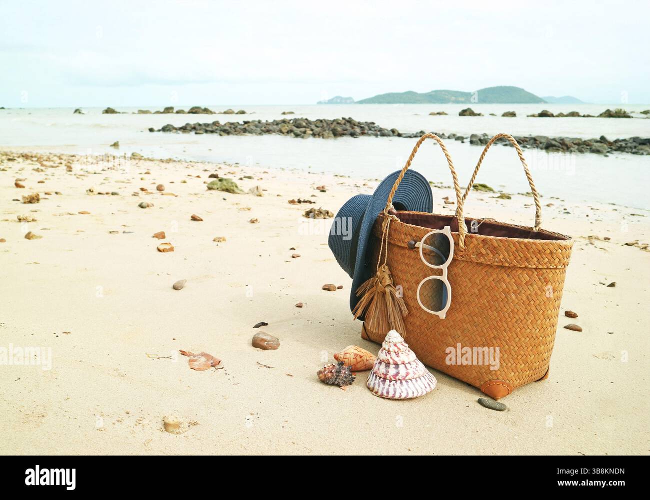 Summer woven bag with blue straw hat and sunglasses on the sandy beach with natural seashells Stock Photo