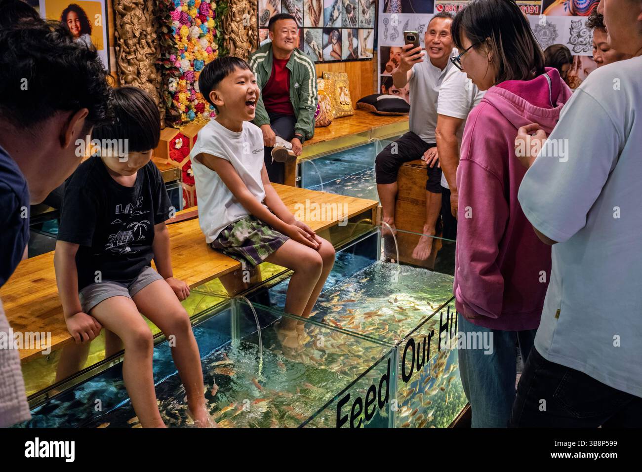 A boy laughing when his feet are tickled by nibbling fish at a fish massage stall, Siem Reap night market, Cambodia Stock Photo