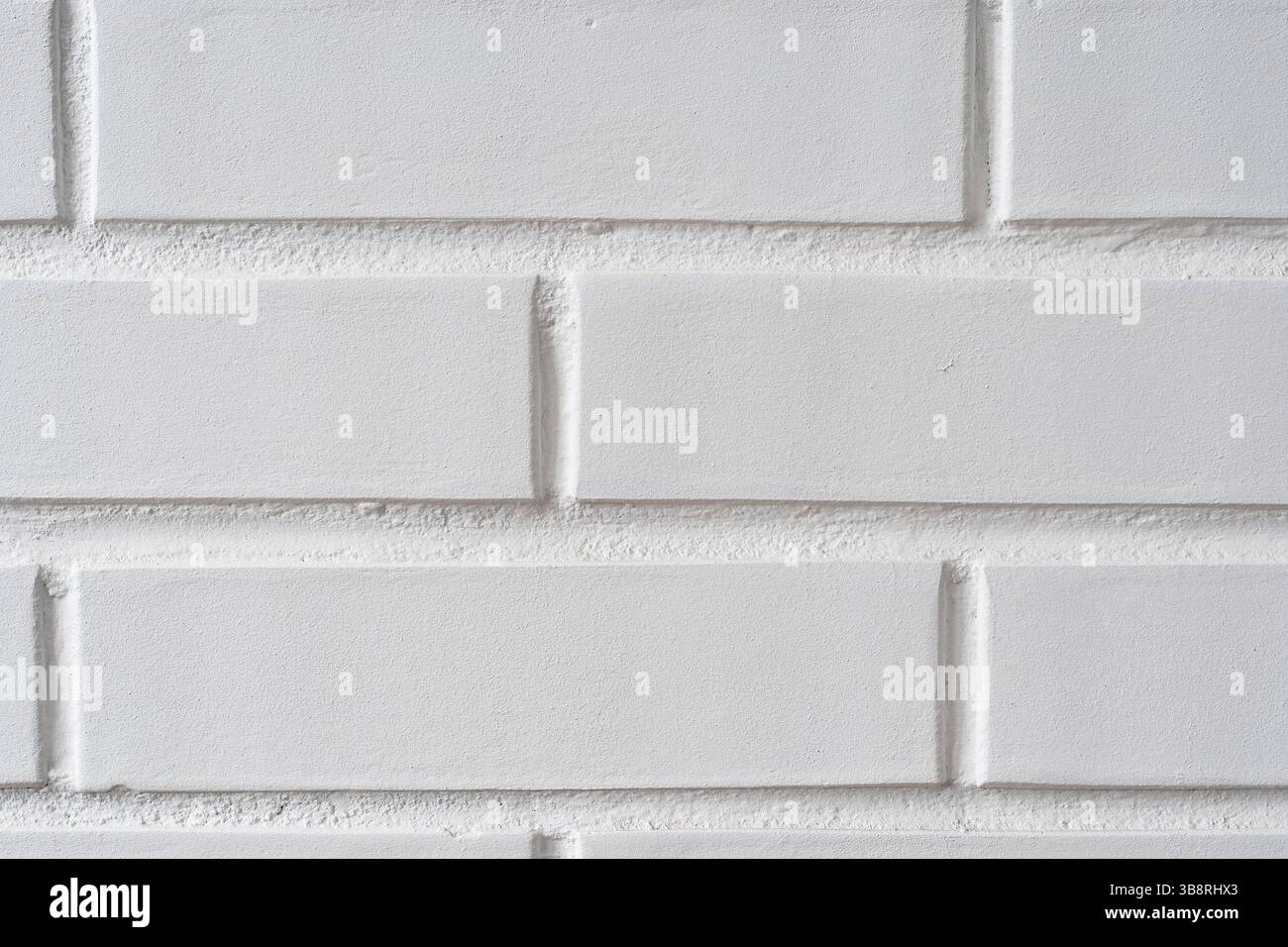 Painted white brick wall providing a minimalistic, textured backdrop. Light catches the rough surface, highlighting the clean lines and geometry Stock Photo