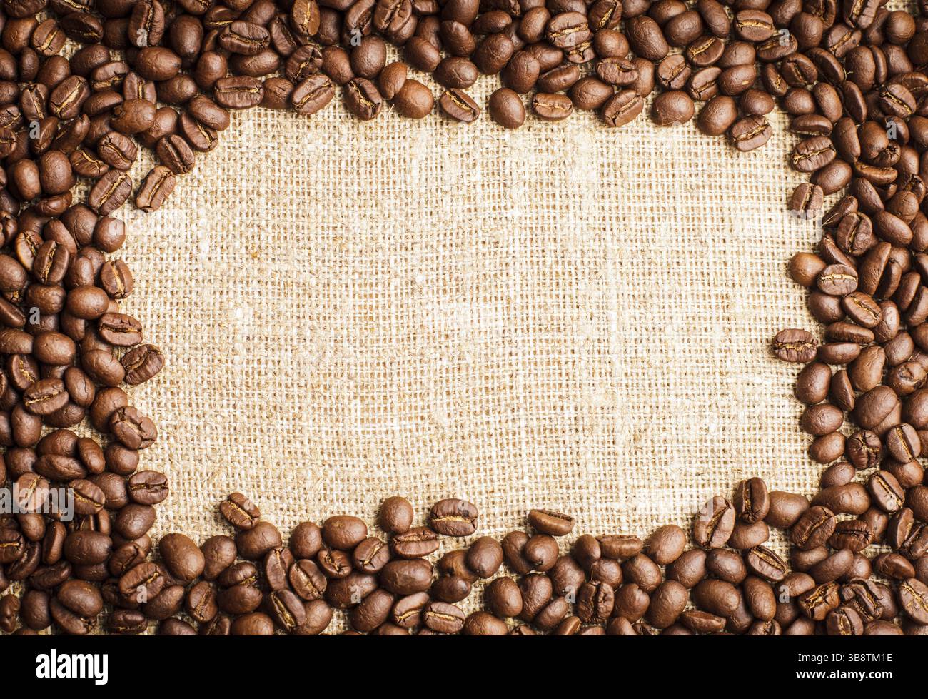 Spilled coffee beans frame over burlap textile Stock Photo
