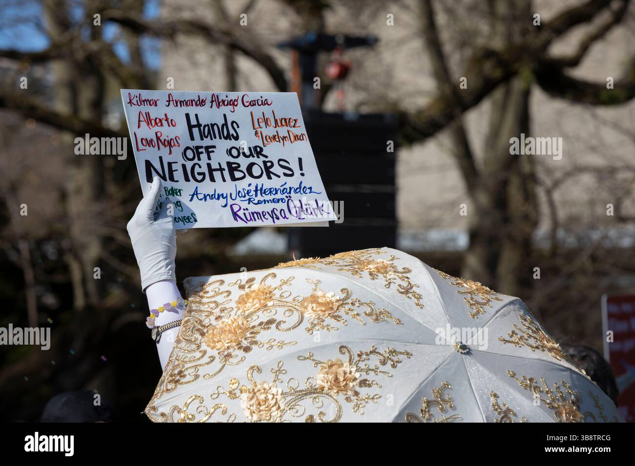 An individual with a fanciful parasol holds up a sign with the names of immigrants who have been targeted by ICE during the “Hands Off” rally at Seatt Stock Photo