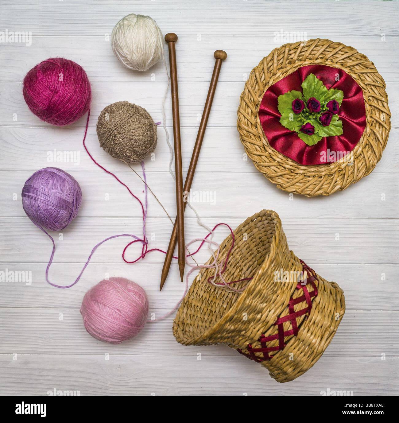 From above the colored balls of yarn in wicker basket with needles on white wooden board in Ukraine Stock Photo