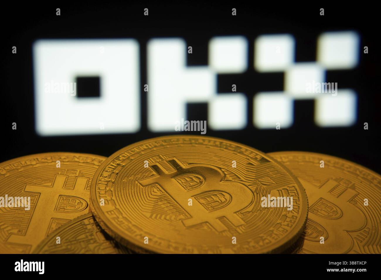 Dhaka, Bangladesh- 04 April 2025: Close-up of Bitcoin coins with the OKX logo visible on a screen in the background Stock Photo