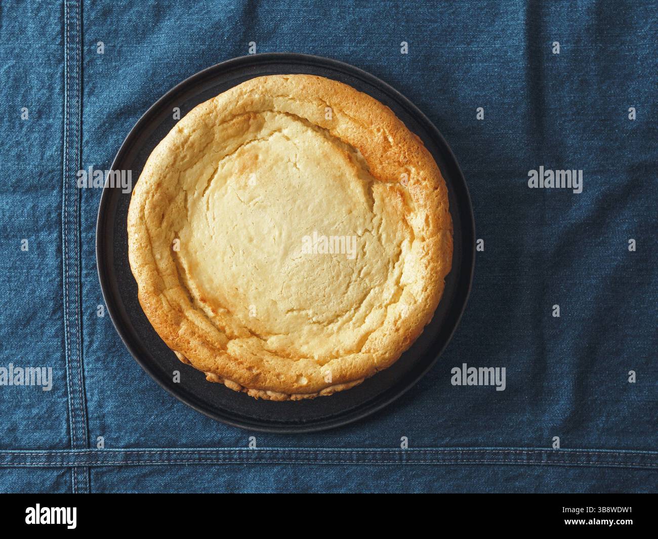 Plate with whole cheesecake pie on table with jeans tablecloth. Classic cheesecake flat lay or top view. Vertical Stock Photo