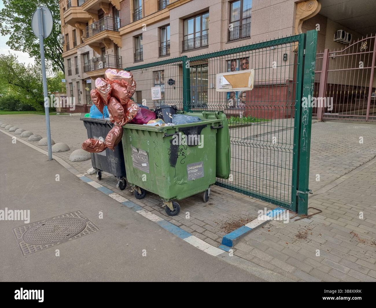 Shiny metallic heart-shaped party balloons abandoned in waste container; concept of breaking up, lost love, end of relationship, end of the party - Smartphone Captured Stock Image