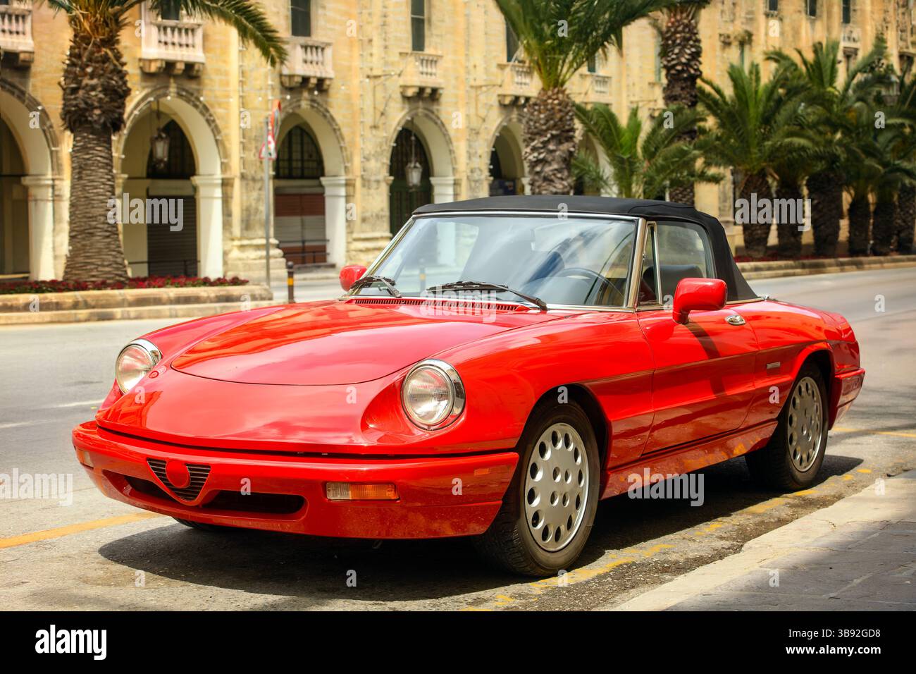 Vintage red car parked on a city street with palm trees and old ...