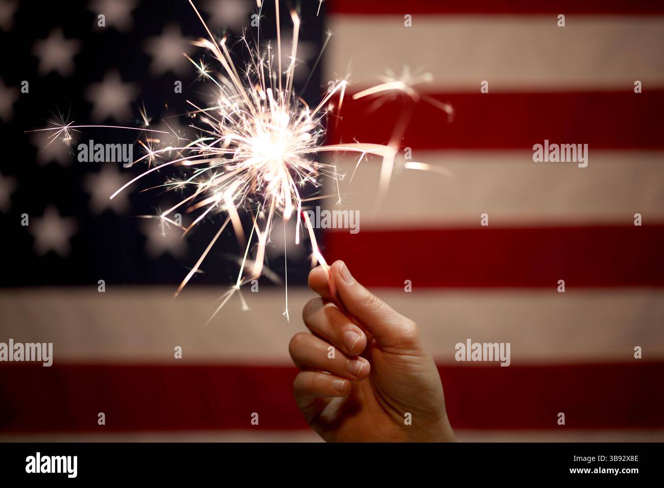 Hand holding lit sparkler in front of the American Flag for 4th of July ...
