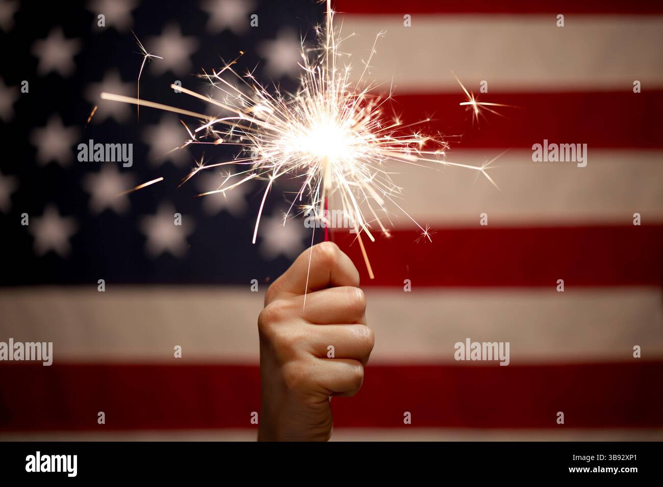 Hand holding lit sparkler in front of the American Flag for 4th of July ...