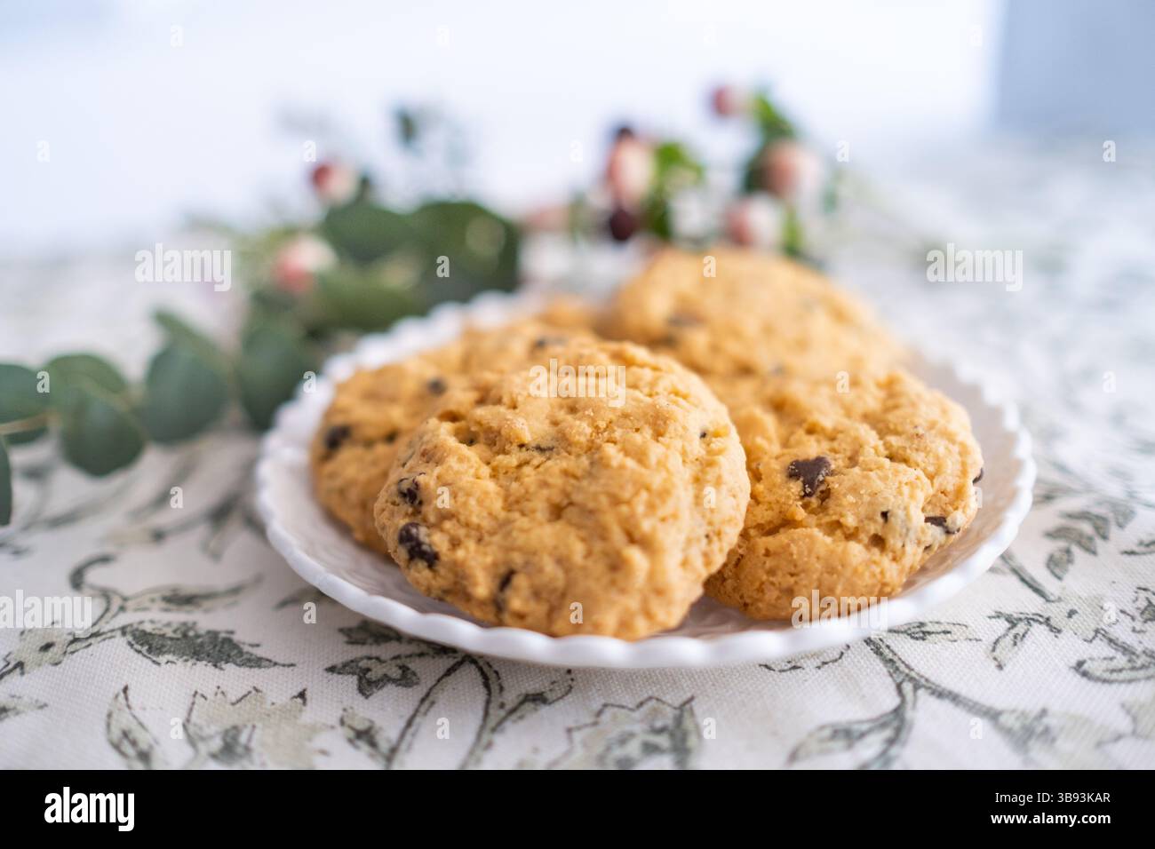 Detail of a small wicker plate with some delicious chocolate chips gluten free cookies decorated with flowers. They are fresh, baked and handmade. The Stock Photo